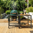 Green outdoor grill on a wooden deck with plants and furniture in the background