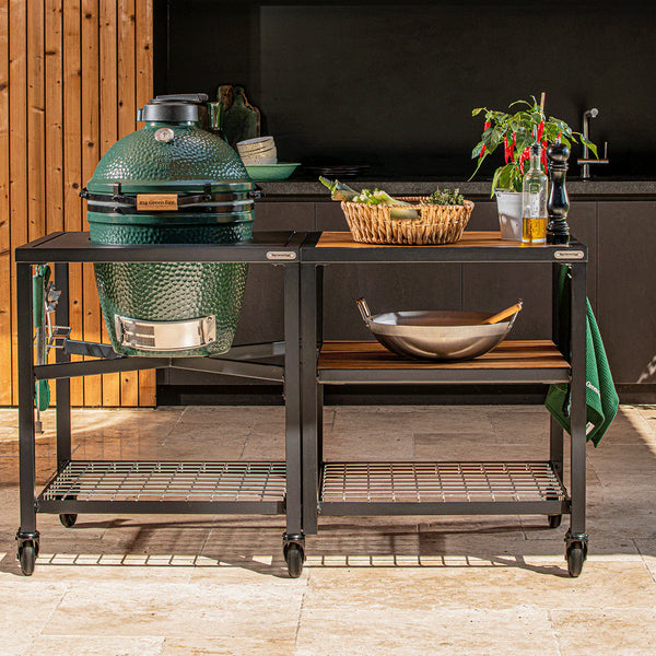 Outdoor kitchen setup with a large green grill on a cart, surrounded by various kitchen items.