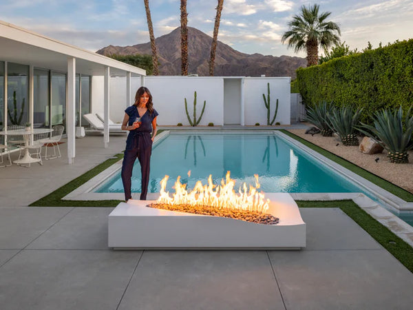 Lumacast Duna - Woman standing by a modern outdoor fire pit with a pool and mountains in the background