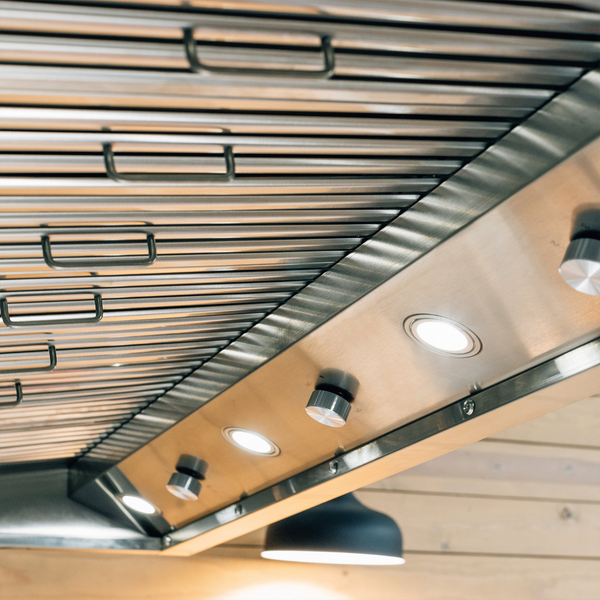 Close-up view of a Summerset stainless steel range hood with lights and controls, mounted on a light-colored wooden ceiling.
