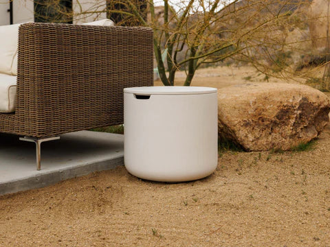Lumacast  White tank with tank cover on a sandy ground with wicker furniture and a tree in the background